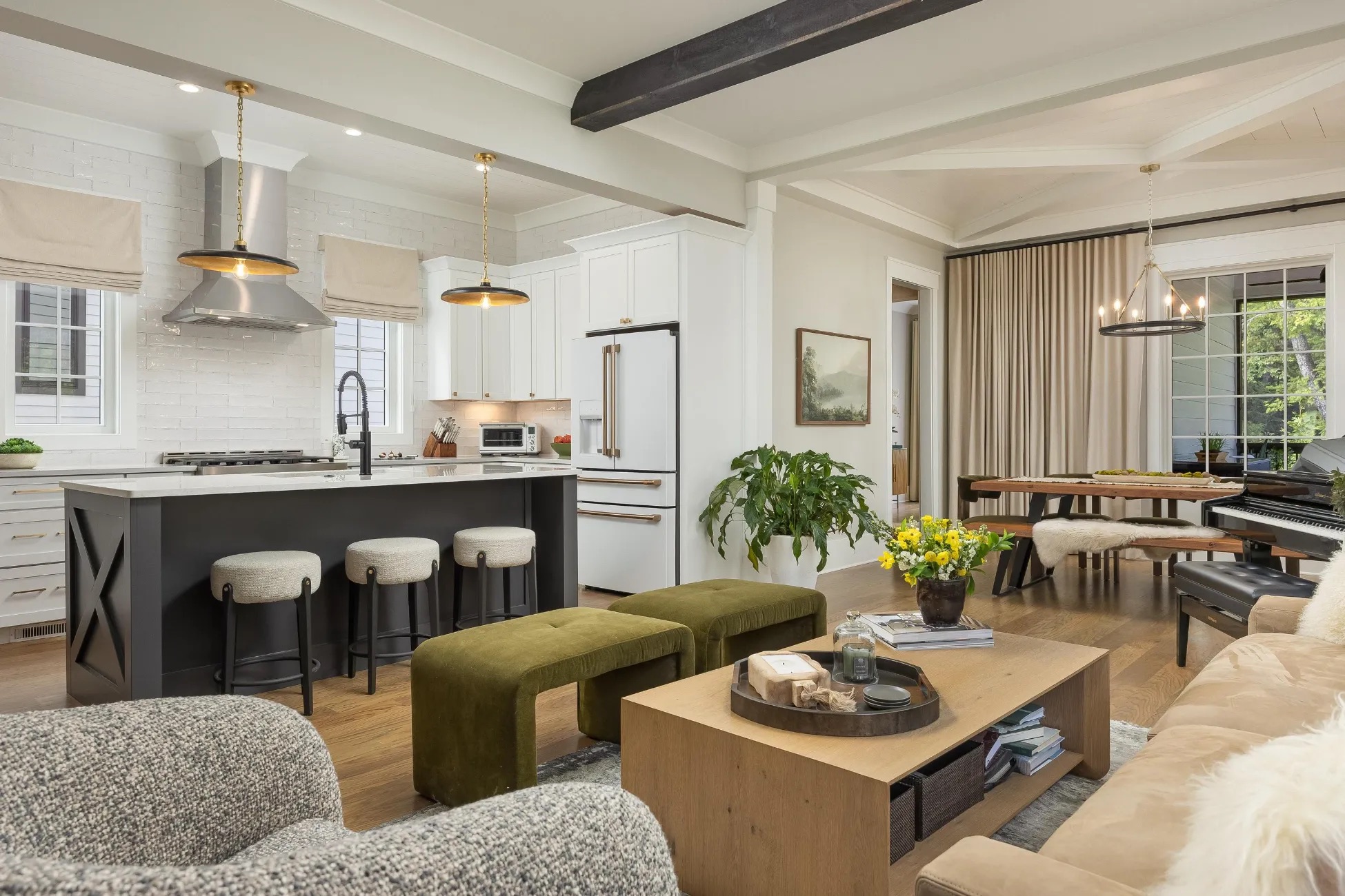 Open-concept living space featuring a modern kitchen with a central island, stools, living area with coffee table, green benches, plants, and a piano near large windows.