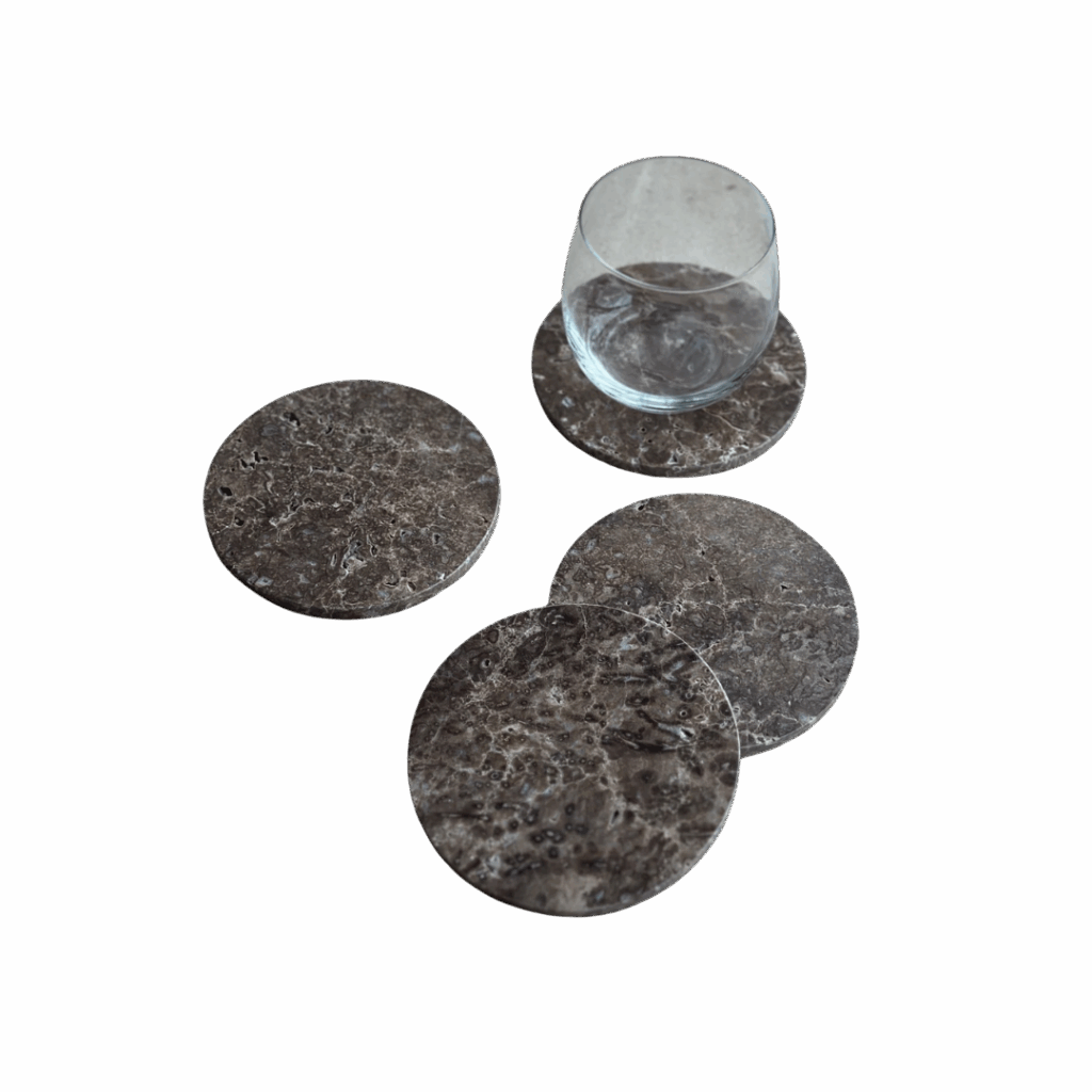 A clear glass sits on one of four round, dark marble coasters arranged on a white surface—an elegant choice for hosting.