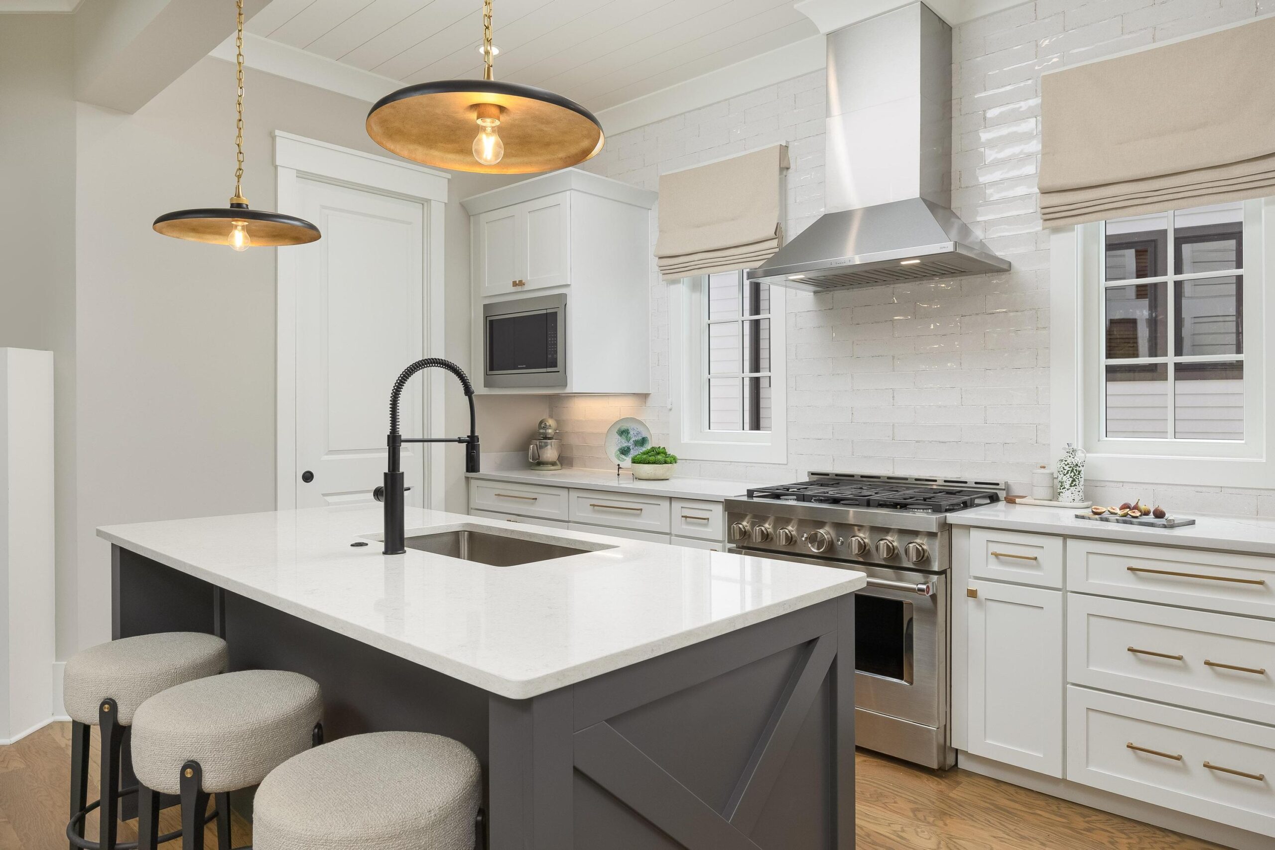Contemporary kitchen featuring white cabinets, stainless steel appliances, a center island with sink and black faucet, pendant lights, and beige window shades—perfect for both everyday cooking and entertaining.