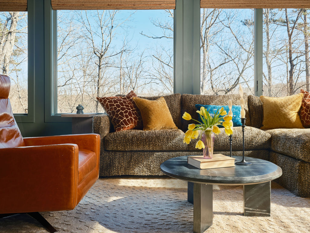 sunlit living room with a brown sofa, orange armchair, round black coffee table