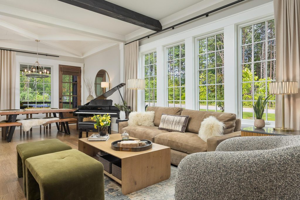 A living room featuring a brown sofa, wooden coffee table, two green ottomans, and a black grand piano in the dining area.